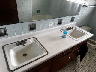 bathroom with toilet, tile walls, double sink vanity, backsplash, and tile patterned flooring