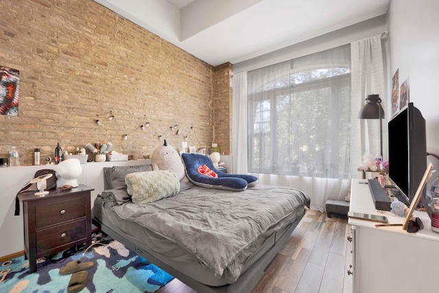 bedroom with hardwood / wood-style floors and brick wall