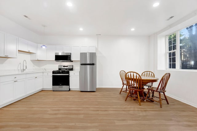 kitchen featuring appliances with stainless steel finishes, sink, pendant lighting, light hardwood / wood-style flooring, and white cabinetry