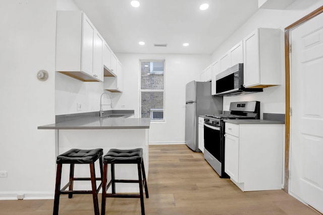 kitchen with white cabinetry, sink, stainless steel appliances, a kitchen bar, and light wood-type flooring