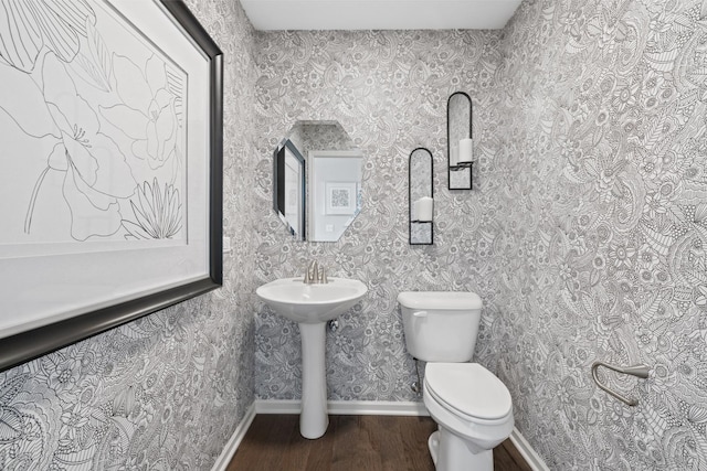 half bathroom featuring wallpapered walls, wood finished floors, toilet, and baseboards