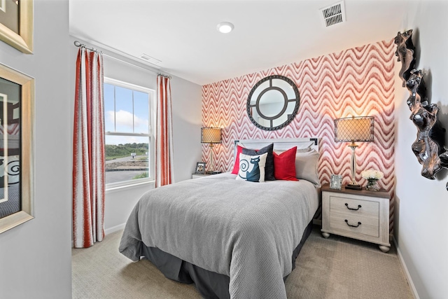 bedroom with light colored carpet, an accent wall, visible vents, baseboards, and wallpapered walls