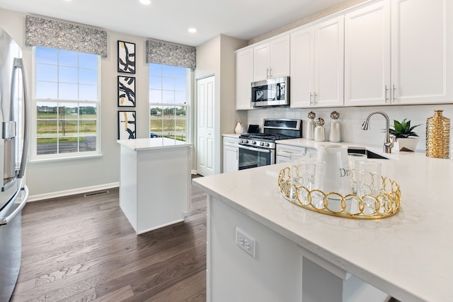 kitchen featuring appliances with stainless steel finishes, sink, white cabinets, dark wood-type flooring, and light stone counters