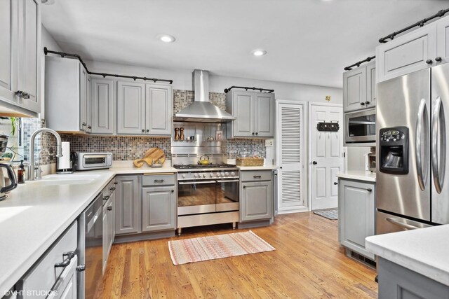 kitchen with decorative backsplash, light hardwood / wood-style floors, appliances with stainless steel finishes, and wall chimney range hood