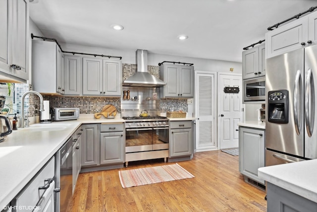 kitchen with gray cabinets, wall chimney exhaust hood, and appliances with stainless steel finishes