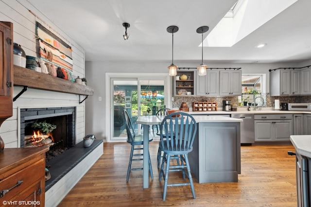 kitchen with gray cabinets, a fireplace, a wealth of natural light, decorative light fixtures, and stainless steel dishwasher