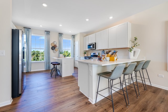 kitchen featuring a breakfast bar, wood-type flooring, white cabinets, a kitchen island, and appliances with stainless steel finishes