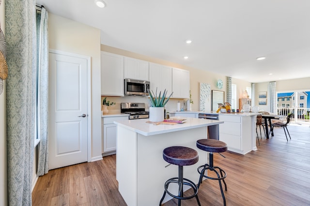 kitchen with white cabinets, kitchen peninsula, a kitchen breakfast bar, light hardwood / wood-style flooring, and appliances with stainless steel finishes