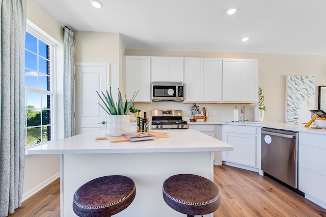 kitchen with appliances with stainless steel finishes, a breakfast bar, light hardwood / wood-style floors, and white cabinetry