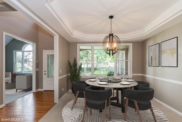 dining space featuring a raised ceiling, hardwood / wood-style floors, an inviting chandelier, and a wealth of natural light