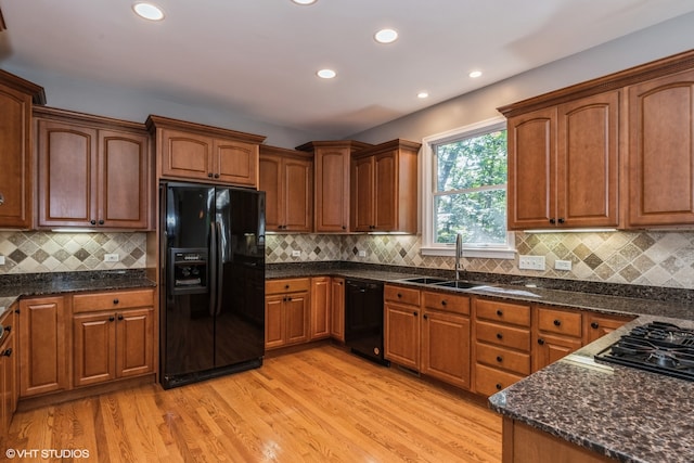 kitchen with tasteful backsplash, sink, black appliances, and light hardwood / wood-style floors