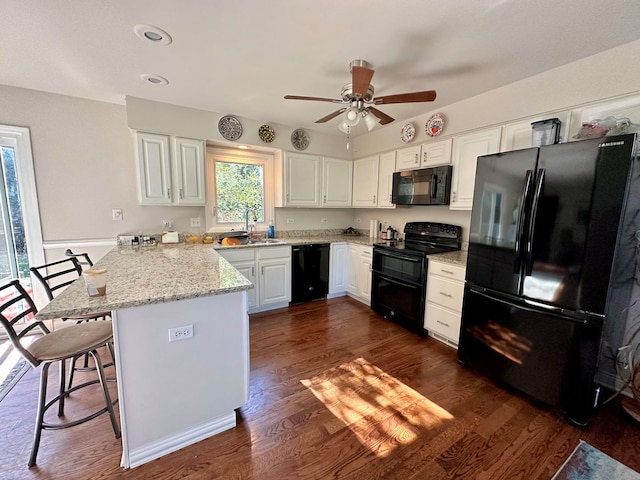 kitchen featuring kitchen peninsula, white cabinetry, black appliances, a breakfast bar area, and dark hardwood / wood-style flooring