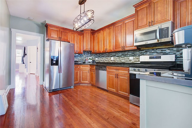 kitchen featuring hanging light fixtures, decorative backsplash, stainless steel appliances, and hardwood / wood-style flooring