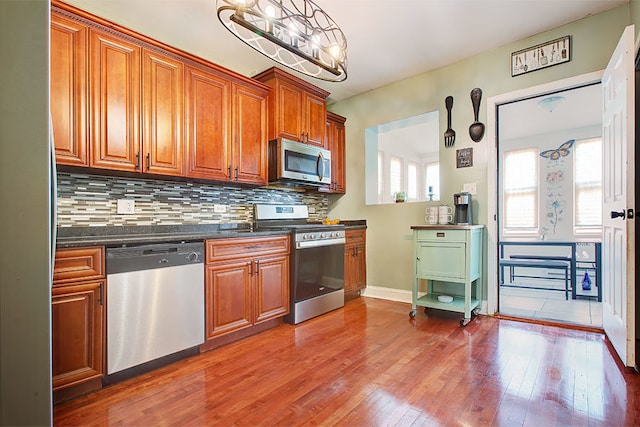 kitchen featuring hanging light fixtures, dark stone countertops, appliances with stainless steel finishes, hardwood / wood-style floors, and backsplash