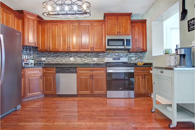 kitchen with appliances with stainless steel finishes, backsplash, light hardwood / wood-style floors, decorative light fixtures, and dark stone counters