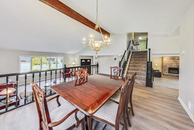 dining space featuring lofted ceiling with beams, a notable chandelier, a fireplace, and light wood-type flooring