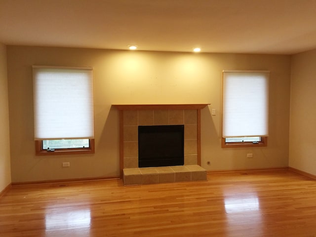 unfurnished living room with a tiled fireplace, light hardwood / wood-style flooring, and a wealth of natural light