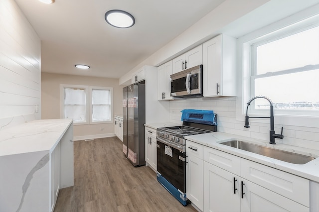 kitchen with appliances with stainless steel finishes, sink, white cabinets, backsplash, and light stone countertops