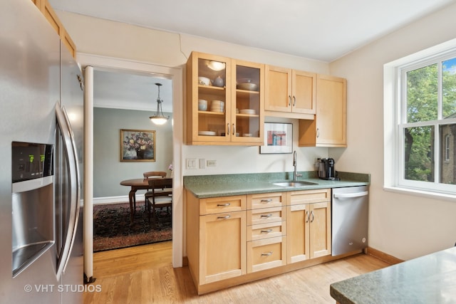 kitchen with light brown cabinetry, stainless steel appliances, hanging light fixtures, sink, and light hardwood / wood-style floors