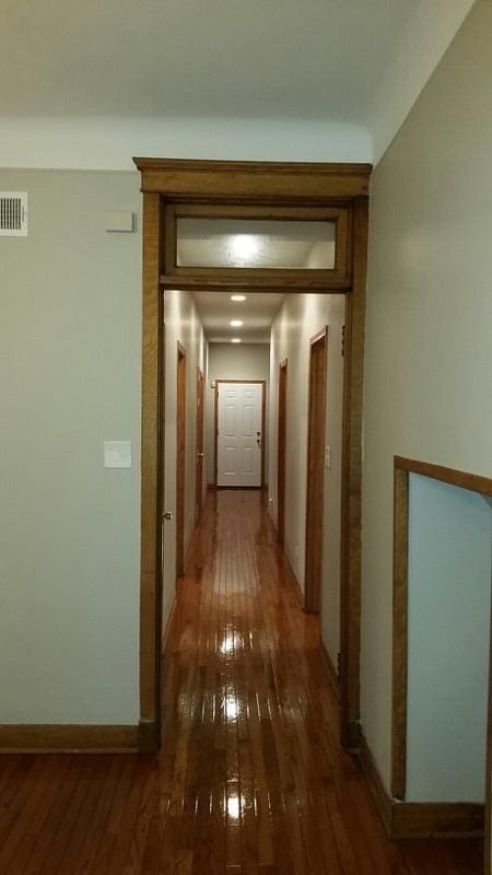 corridor with visible vents, baseboards, and hardwood / wood-style flooring