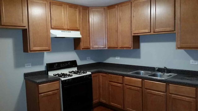 kitchen featuring dark countertops, under cabinet range hood, range with gas stovetop, and a sink