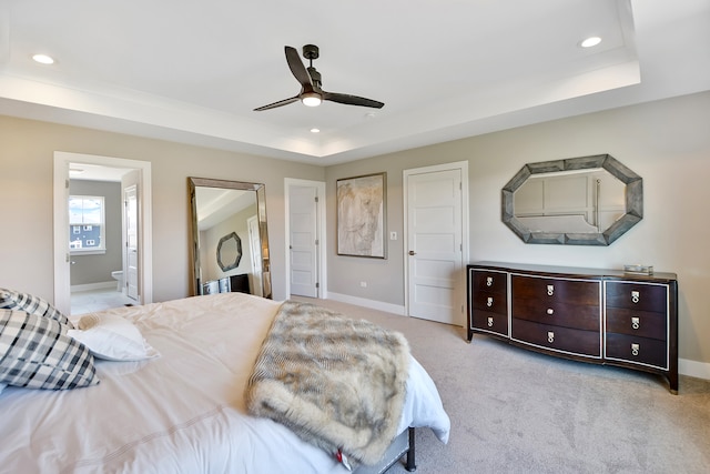 bedroom featuring light carpet, ensuite bathroom, ceiling fan, and a raised ceiling