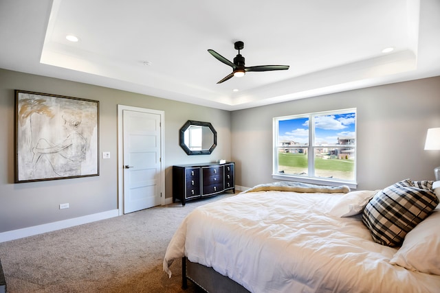 carpeted bedroom with ceiling fan and a raised ceiling