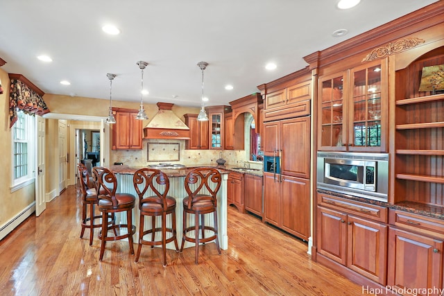 kitchen featuring built in appliances, custom range hood, a center island, light wood-type flooring, and a breakfast bar