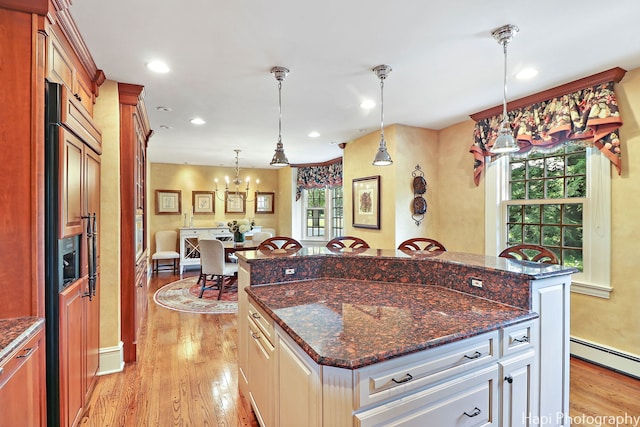 kitchen featuring light hardwood / wood-style flooring, hanging light fixtures, a kitchen island, and dark stone counters