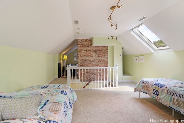 carpeted bedroom with vaulted ceiling with skylight, brick wall, and track lighting