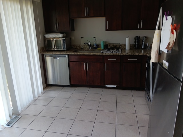 kitchen with dark stone counters, stainless steel appliances, sink, dark brown cabinets, and light tile patterned floors