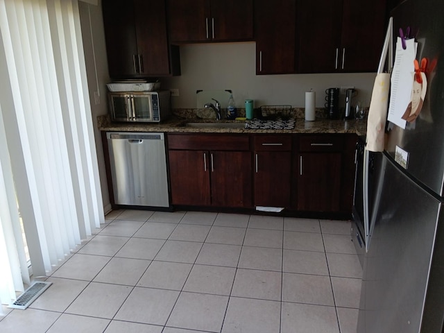 kitchen with dark stone countertops, sink, stainless steel appliances, and light tile patterned flooring