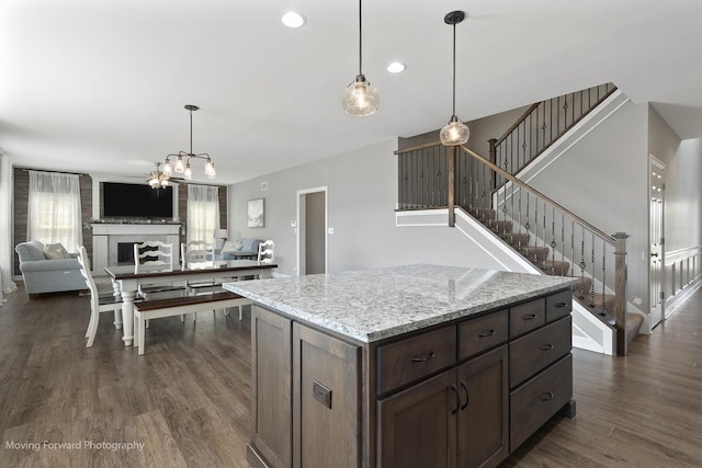 kitchen with hanging light fixtures, light stone countertops, dark brown cabinets, and dark hardwood / wood-style floors