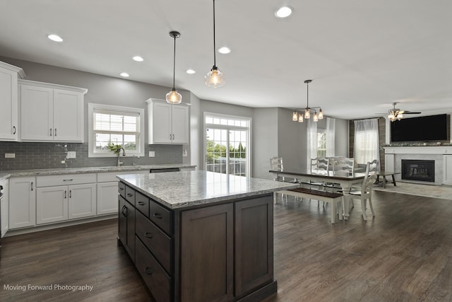 kitchen with pendant lighting, white cabinetry, backsplash, light stone counters, and dark wood-type flooring