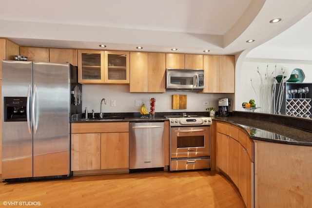 kitchen with kitchen peninsula, sink, dark stone countertops, light hardwood / wood-style floors, and stainless steel appliances