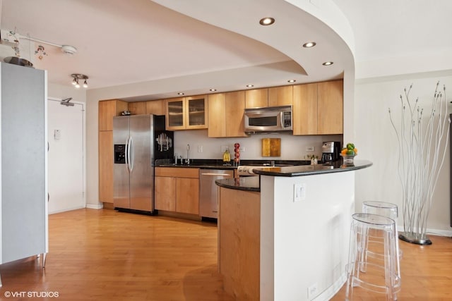 kitchen featuring kitchen peninsula, light wood-type flooring, sink, and appliances with stainless steel finishes