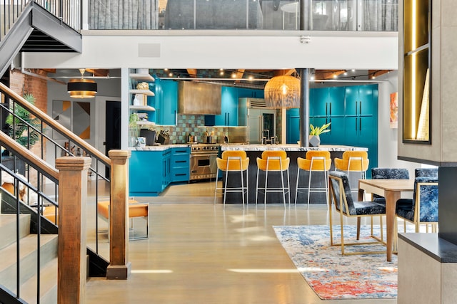 bar with blue cabinets, high end appliances, light hardwood / wood-style flooring, a towering ceiling, and backsplash