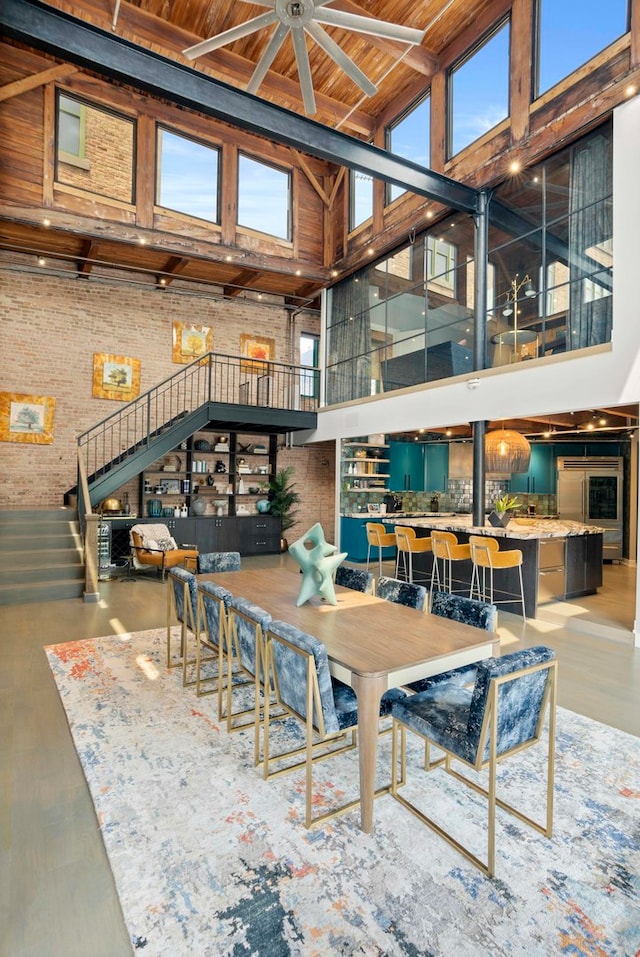 dining room featuring wood ceiling, a towering ceiling, ceiling fan, and brick wall