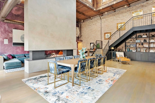 dining area with a towering ceiling, wood-type flooring, brick wall, and a multi sided fireplace