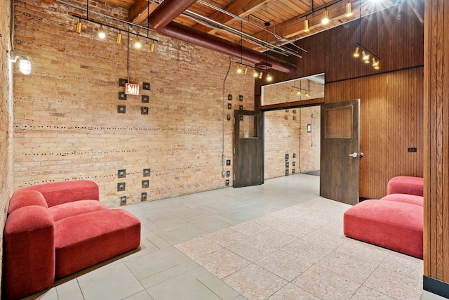 interior space featuring rail lighting, wooden walls, beamed ceiling, brick wall, and a high ceiling