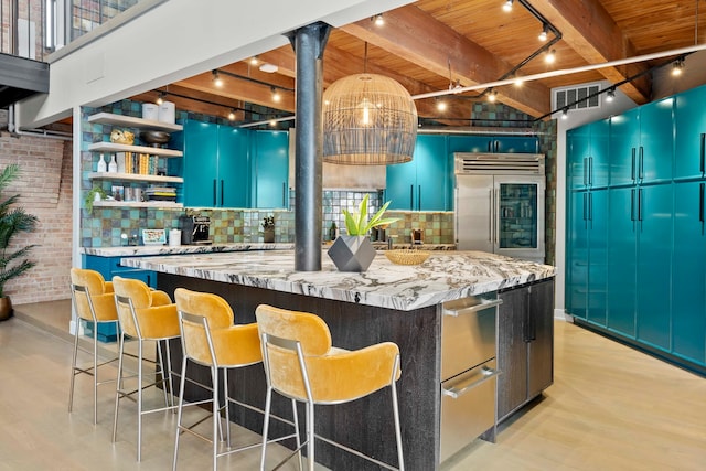 kitchen with blue cabinetry, built in refrigerator, a center island, light stone countertops, and brick wall