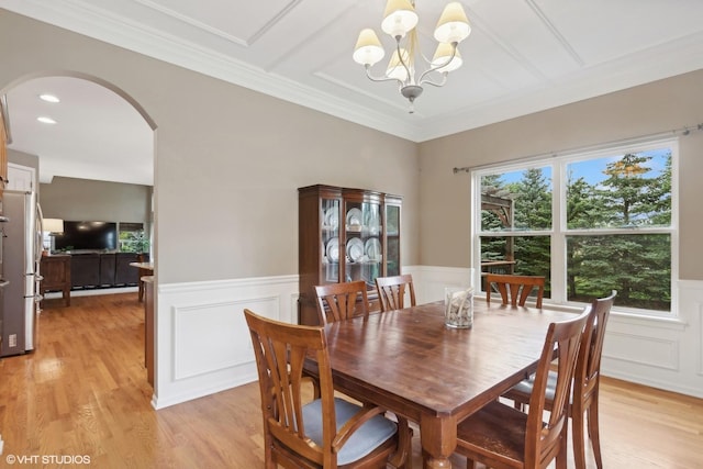 dining area featuring a wainscoted wall, ornamental molding, an inviting chandelier, light wood-style floors, and arched walkways