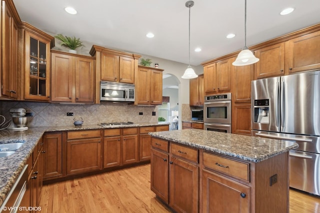 kitchen featuring brown cabinetry, arched walkways, and stainless steel appliances