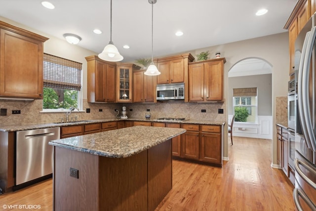 kitchen with arched walkways, brown cabinets, stainless steel appliances, and a sink