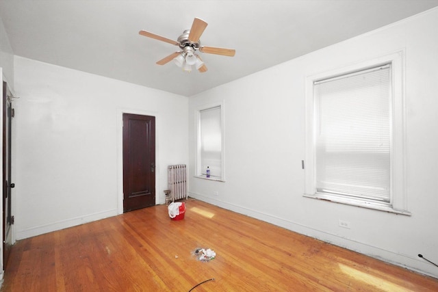 unfurnished bedroom featuring baseboards, wood finished floors, a ceiling fan, and radiator