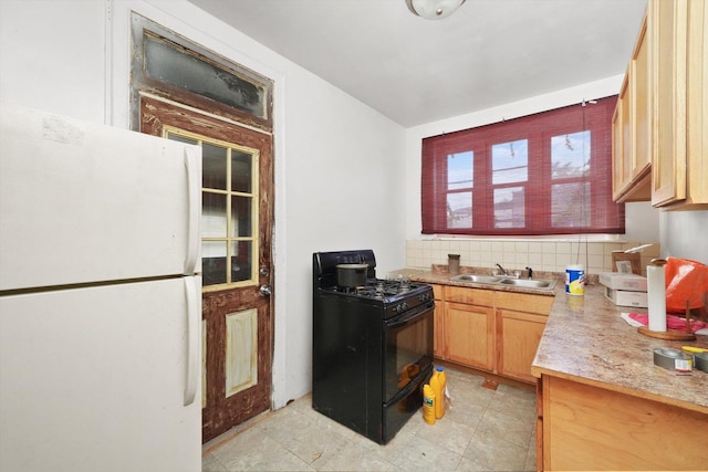 kitchen featuring black range with gas cooktop, decorative backsplash, freestanding refrigerator, light countertops, and a sink