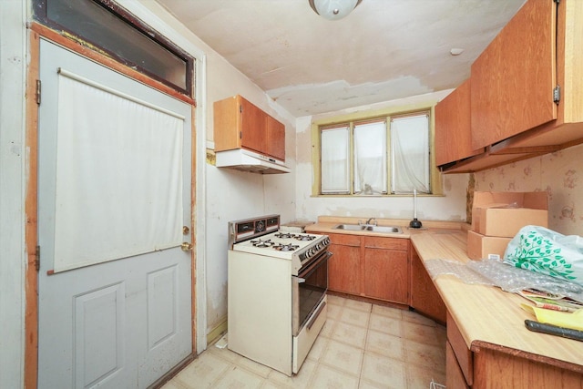 kitchen with under cabinet range hood, white gas range, light countertops, and brown cabinetry