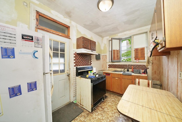 kitchen featuring brown cabinets, gas range oven, freestanding refrigerator, a sink, and under cabinet range hood