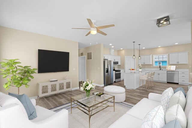 living room featuring ceiling fan, sink, and light wood-type flooring