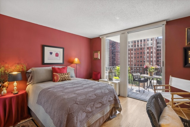 bedroom featuring expansive windows, access to outside, a textured ceiling, and light hardwood / wood-style flooring